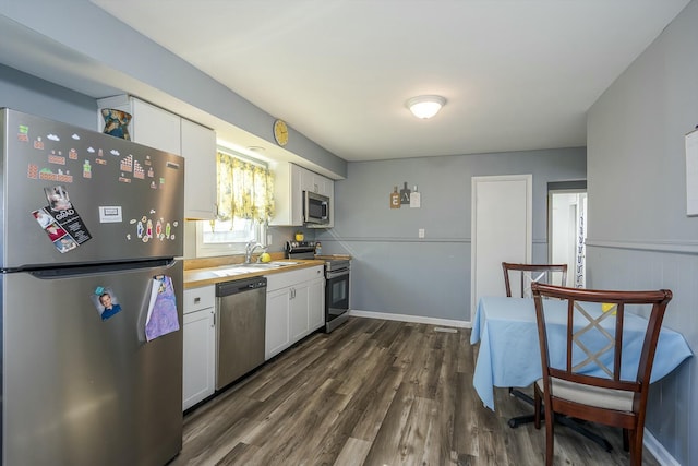 kitchen with stainless steel appliances, dark wood-type flooring, white cabinets, a sink, and baseboards