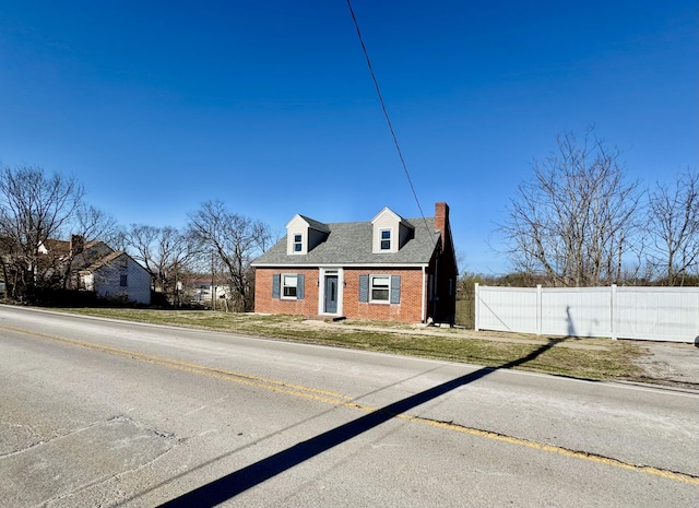 new england style home featuring a shingled roof, brick siding, fence, and a chimney