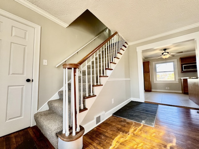 stairway with baseboards, a textured ceiling, ornamental molding, and wood finished floors