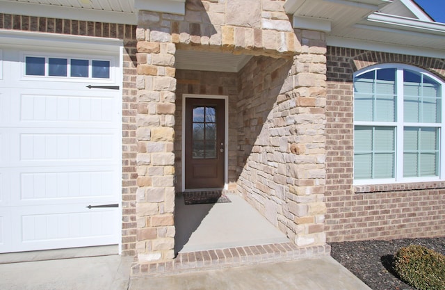 view of exterior entry featuring an attached garage, stone siding, and brick siding