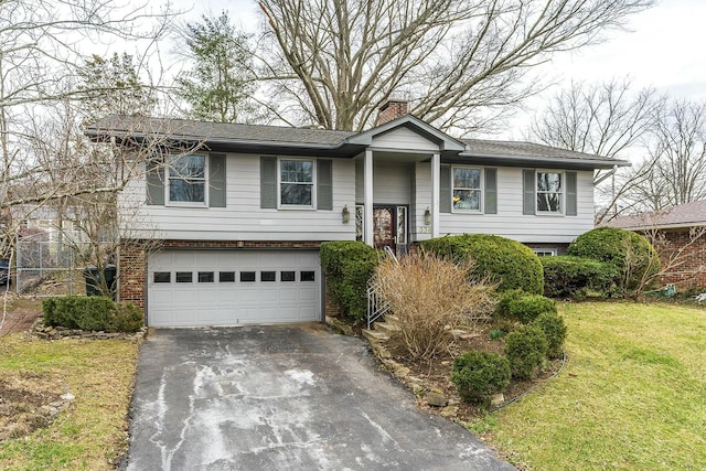 bi-level home with aphalt driveway, an attached garage, brick siding, a chimney, and a front yard