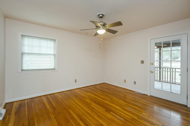 spare room featuring a ceiling fan, visible vents, wood finished floors, and baseboards