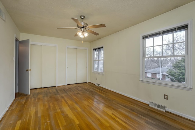 unfurnished bedroom featuring visible vents, two closets, a textured ceiling, hardwood / wood-style floors, and baseboards