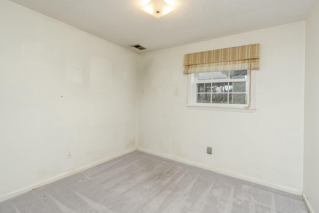 carpeted spare room featuring visible vents, baseboards, and a textured ceiling
