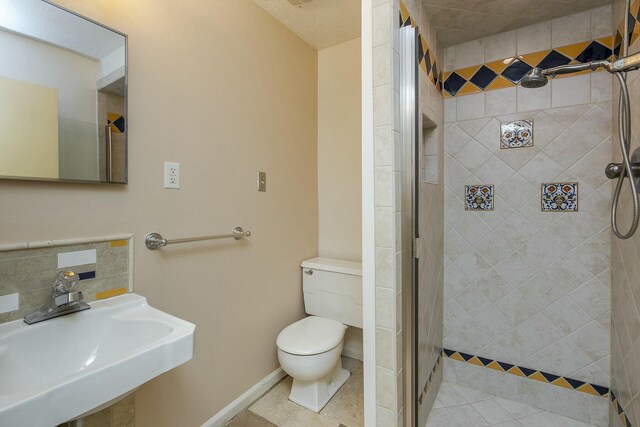 bathroom featuring baseboards, a sink, a shower stall, tile patterned floors, and toilet