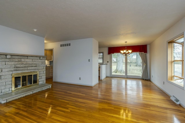 unfurnished living room with visible vents, light wood finished floors, an inviting chandelier, a fireplace, and a textured ceiling