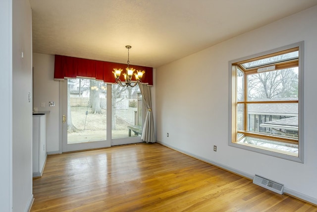 unfurnished dining area featuring light wood-style floors, visible vents, baseboards, and a notable chandelier