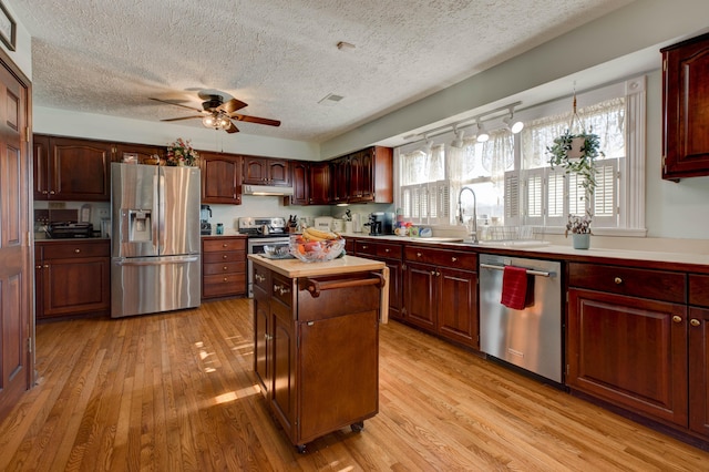 kitchen featuring under cabinet range hood, light wood-style flooring, stainless steel appliances, and a center island