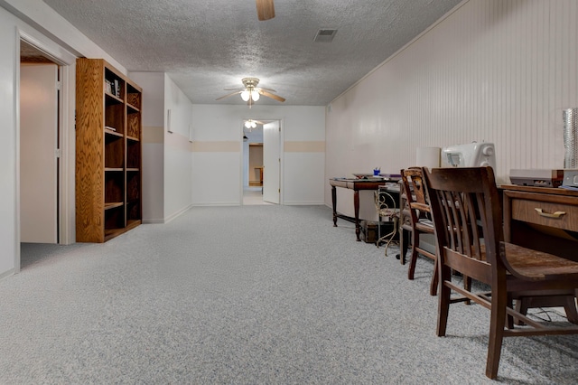 carpeted home office with a textured ceiling, visible vents, and a ceiling fan