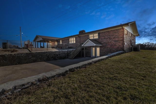 rear view of property with cooling unit, brick siding, fence, a lawn, and a chimney