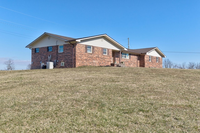 back of property featuring brick siding, a yard, and central AC