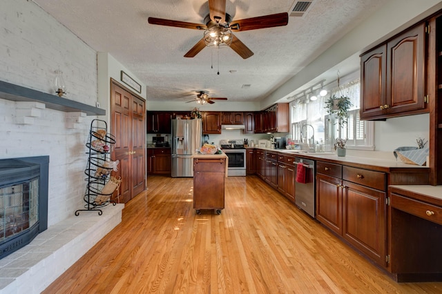 kitchen featuring a kitchen island, under cabinet range hood, stainless steel appliances, light wood-type flooring, and a brick fireplace