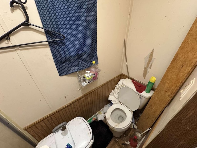 bathroom with a wainscoted wall, wood walls, and toilet