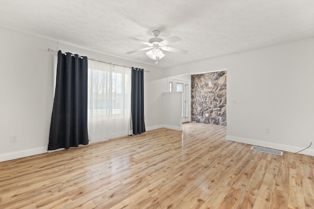 empty room featuring light wood-type flooring, a ceiling fan, visible vents, and a textured ceiling