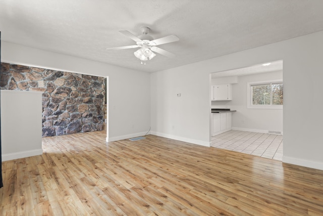 unfurnished living room featuring a textured ceiling, ceiling fan, baseboards, and light wood-style floors