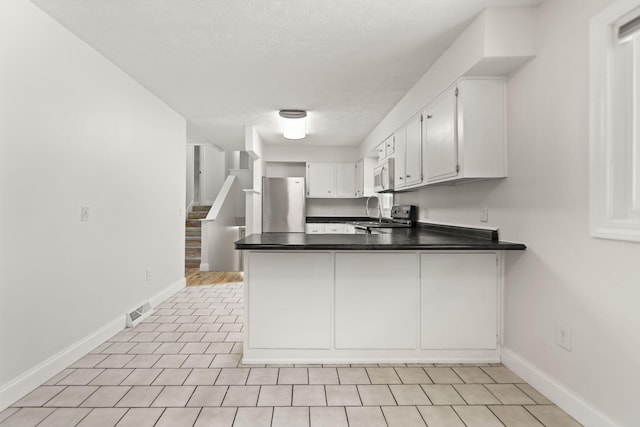 kitchen featuring dark countertops, visible vents, appliances with stainless steel finishes, white cabinets, and a peninsula