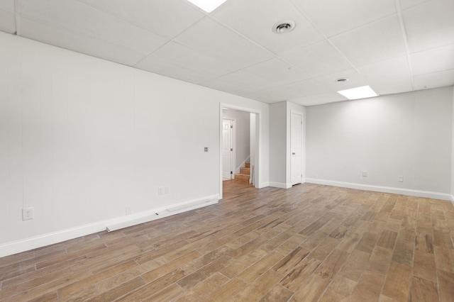 empty room with a paneled ceiling, visible vents, wood finished floors, baseboards, and stairs