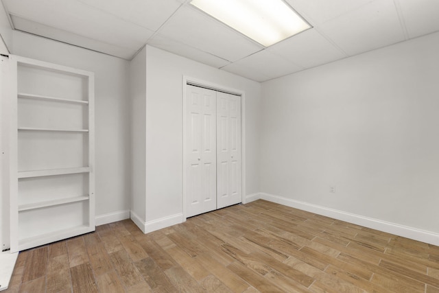 unfurnished bedroom featuring light wood-style floors, baseboards, a drop ceiling, and a closet