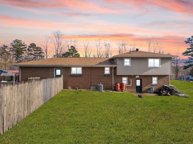 rear view of house featuring brick siding, a lawn, and fence