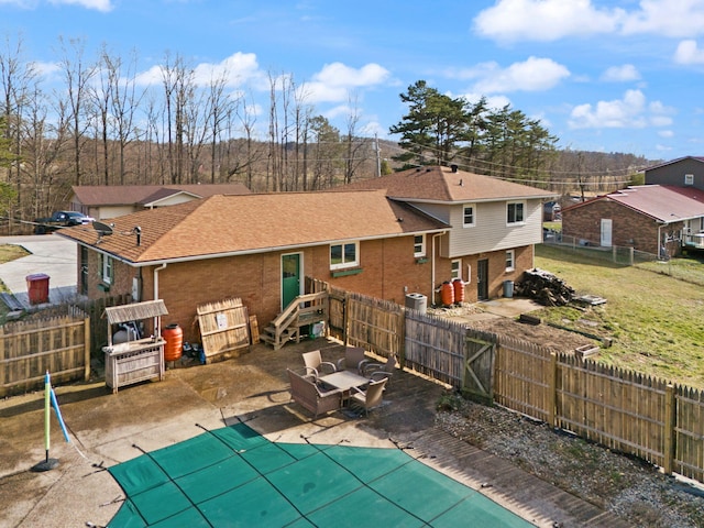 back of house featuring brick siding, roof with shingles, a fenced backyard, and a fenced in pool