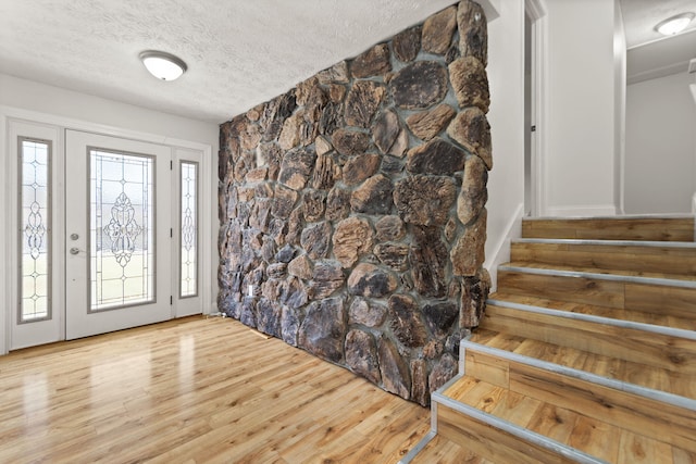 entryway featuring a textured ceiling, stairs, and light wood-style floors