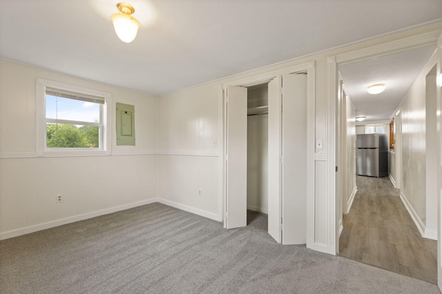 unfurnished bedroom featuring baseboards, a closet, freestanding refrigerator, and light colored carpet