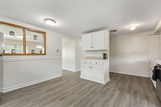 clothes washing area featuring a wainscoted wall, wood finished floors, visible vents, and baseboards