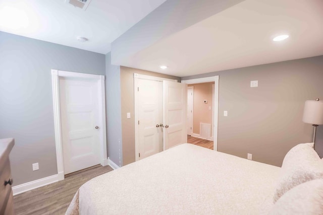 bedroom with recessed lighting, wood finished floors, visible vents, baseboards, and a closet