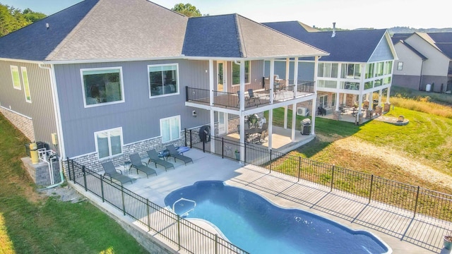 rear view of property featuring a fenced in pool, a patio area, a lawn, and a balcony