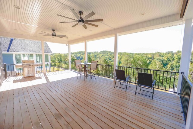 deck with a forest view, ceiling fan, outdoor dining area, and area for grilling