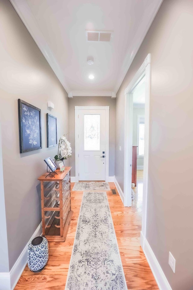 doorway to outside with ornamental molding, light wood finished floors, visible vents, and baseboards