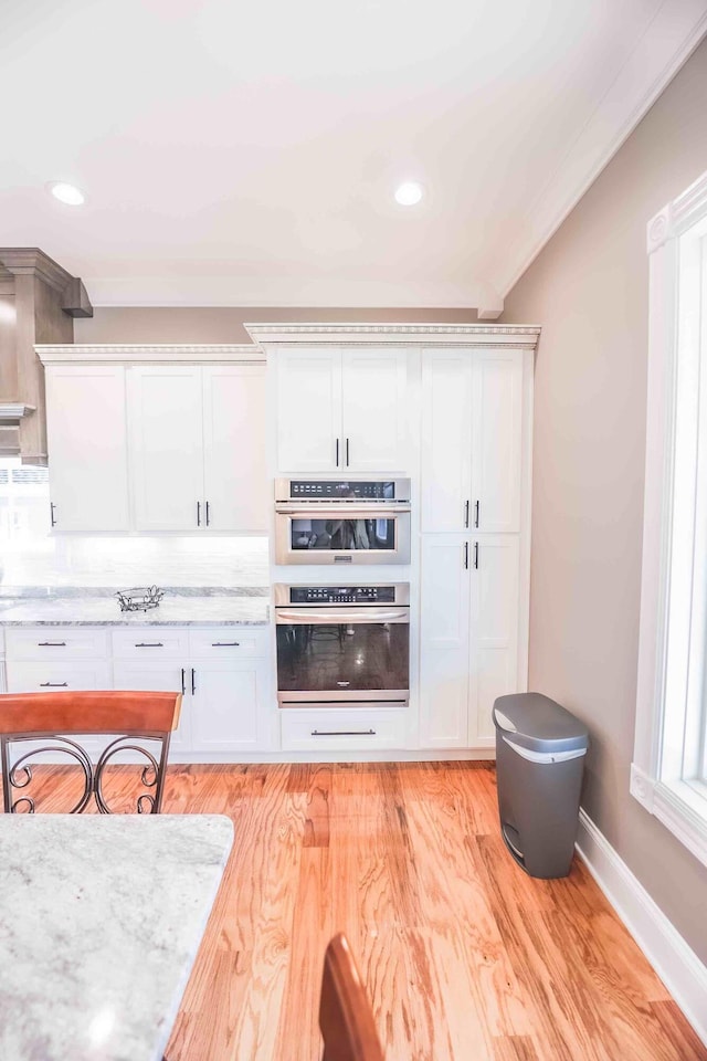 kitchen with light wood-style flooring, light stone countertops, white cabinetry, baseboards, and decorative backsplash