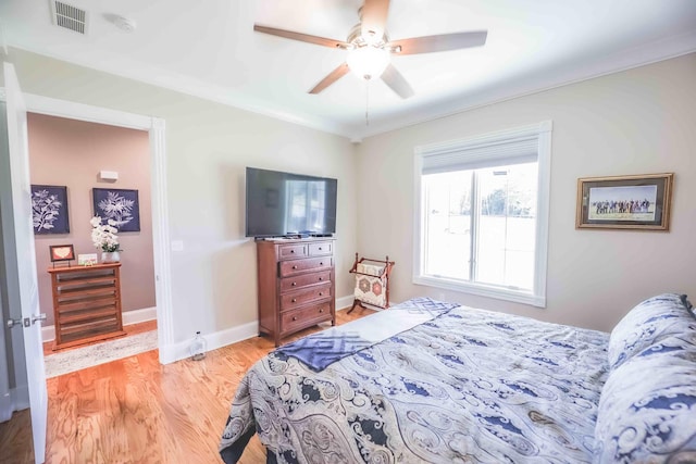 bedroom featuring light wood finished floors, visible vents, ornamental molding, ceiling fan, and baseboards