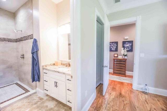 bathroom featuring visible vents, a tile shower, vanity, wood finished floors, and baseboards