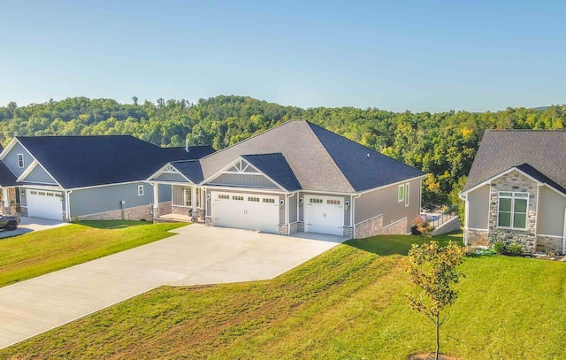 view of front facade featuring a view of trees, concrete driveway, stone siding, an attached garage, and a front lawn