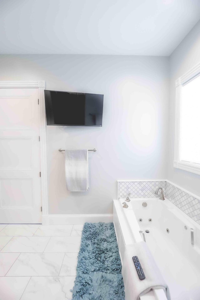 bathroom with marble finish floor, a tub with jets, and baseboards