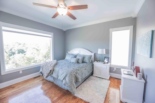 bedroom with light wood-type flooring, a ceiling fan, baseboards, and crown molding