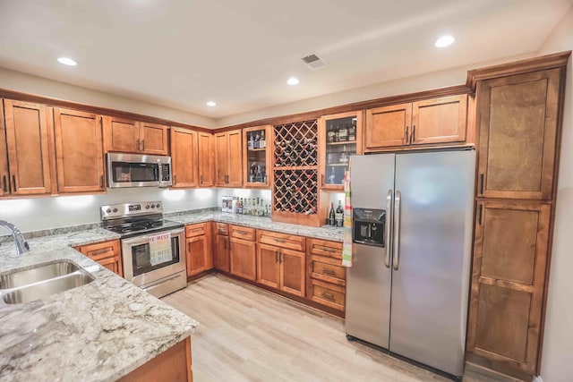 kitchen featuring stainless steel appliances, brown cabinets, glass insert cabinets, and a sink