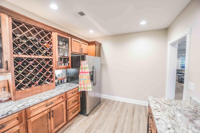 kitchen featuring light stone counters, brown cabinetry, glass insert cabinets, and stainless steel fridge with ice dispenser