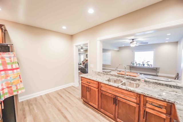 kitchen featuring light wood-type flooring, light stone counters, brown cabinetry, and a sink