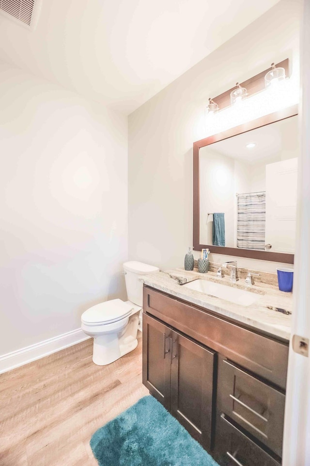 bathroom featuring toilet, wood finished floors, vanity, visible vents, and baseboards