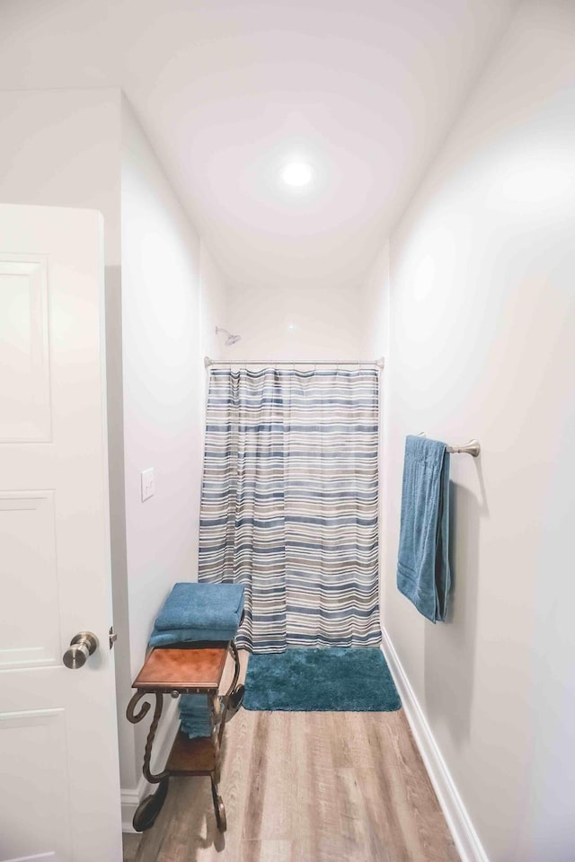 bathroom with baseboards, wood finished floors, and a shower with shower curtain