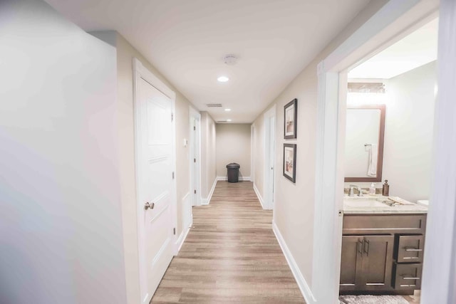 hallway featuring recessed lighting, a sink, baseboards, and wood finished floors