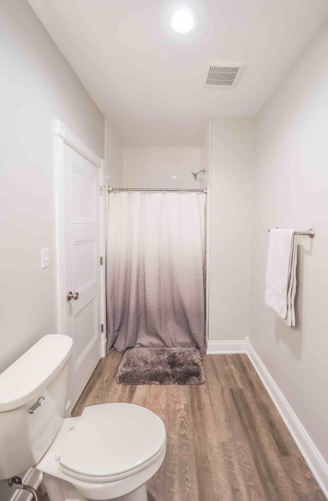 bathroom featuring toilet, a shower with shower curtain, wood finished floors, visible vents, and baseboards