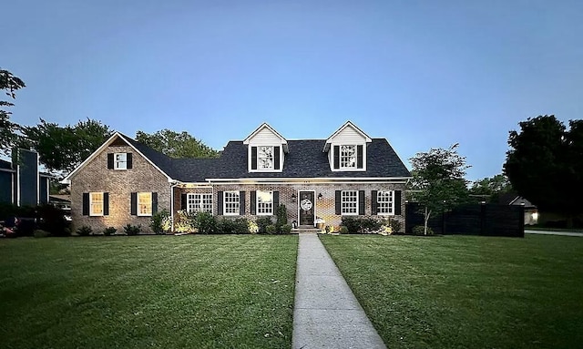 cape cod house featuring brick siding and a front yard