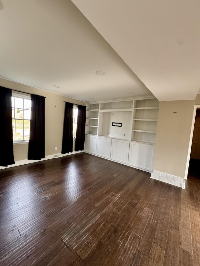 unfurnished living room featuring dark wood-style floors, built in shelves, baseboards, and a healthy amount of sunlight