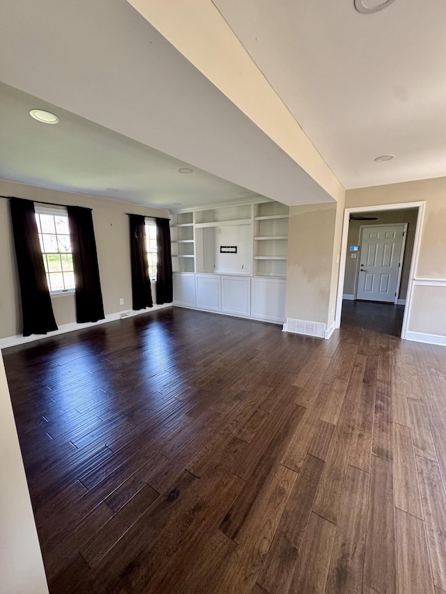 unfurnished living room with dark wood-type flooring, visible vents, baseboards, and built in shelves