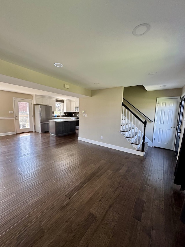unfurnished living room featuring stairway, baseboards, and dark wood finished floors