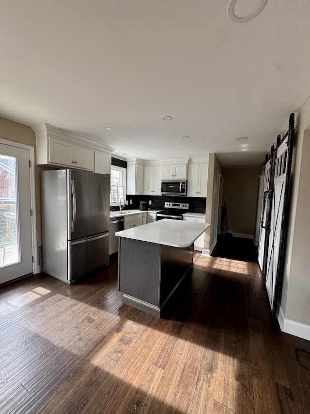 kitchen with a barn door, white cabinets, a kitchen island, stainless steel appliances, and light countertops