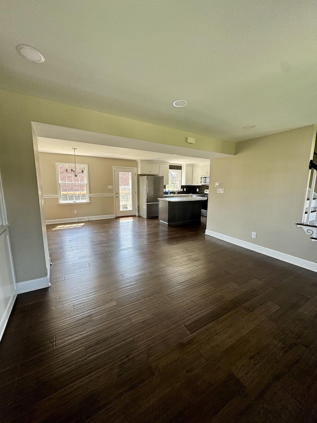 unfurnished living room featuring baseboards, a notable chandelier, and dark wood-style floors